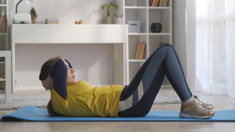 home-fitness-and-workout-young-woman-is-doing-physical-exercise-for-abdominal-muscles-lying-on-floor-and-lifting-torso-side-view-on-body